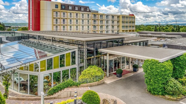 A hotel with a glass conservatory, a red and yellow building, and a well-maintained garden.