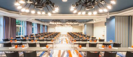 Un salón de conferencias con filas de mesas y sillas, equipado con iluminación en el techo y una alfombra estampada.