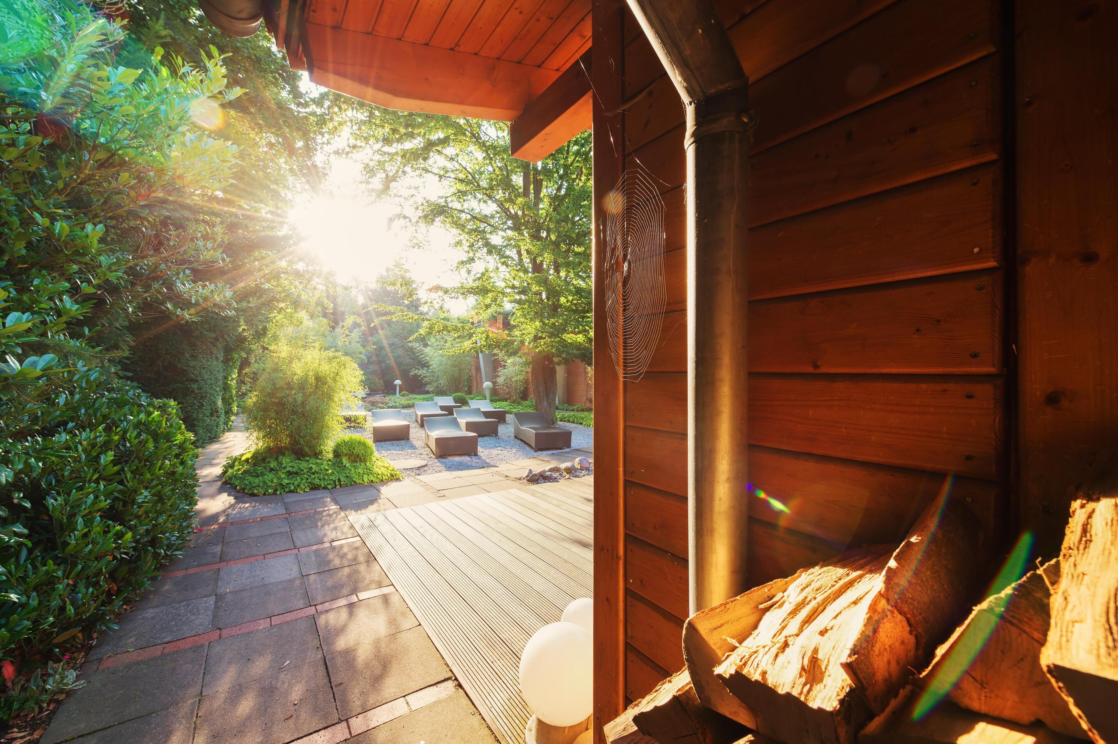 Eine Holzterrasse mit Sitzgelegenheiten im Freien, umgeben von Grünpflanzen und einem Holzgebäude.