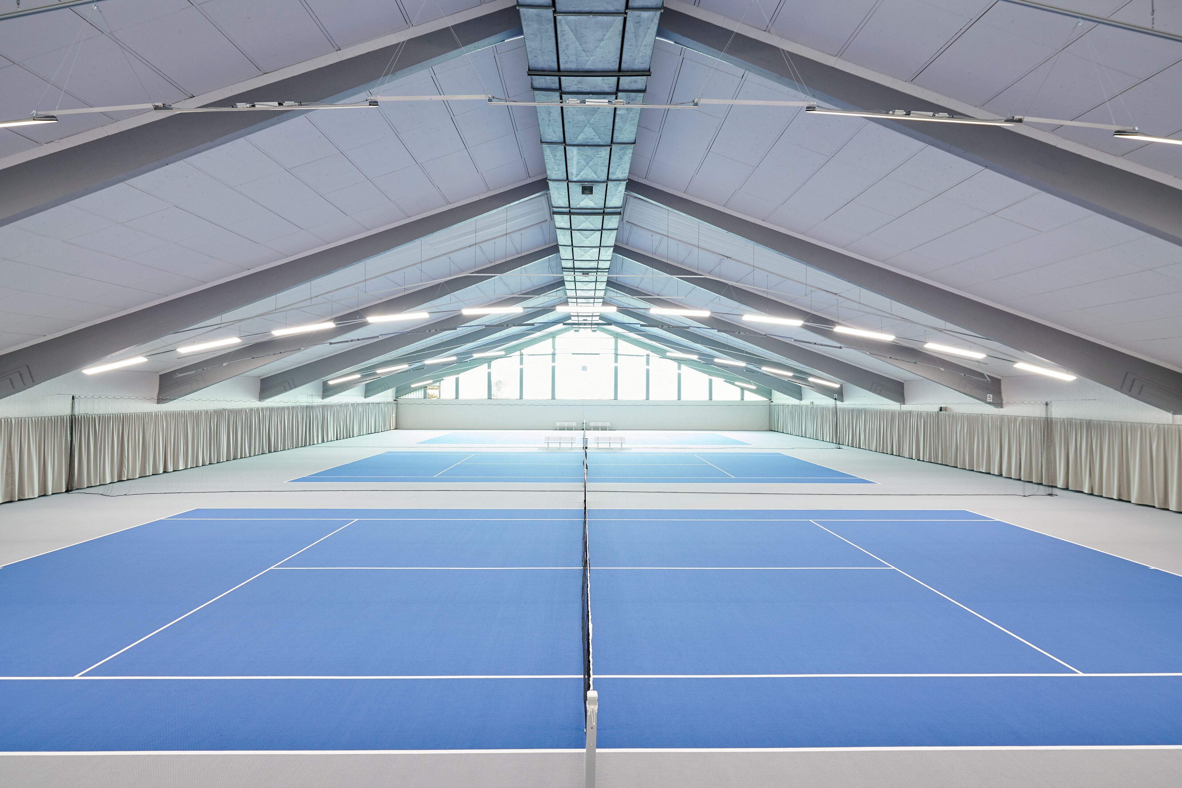 Pista de tenis interior con techo alto y tragaluces.