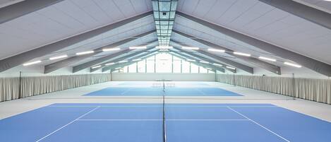 Pista de tenis interior con techo alto y tragaluces.