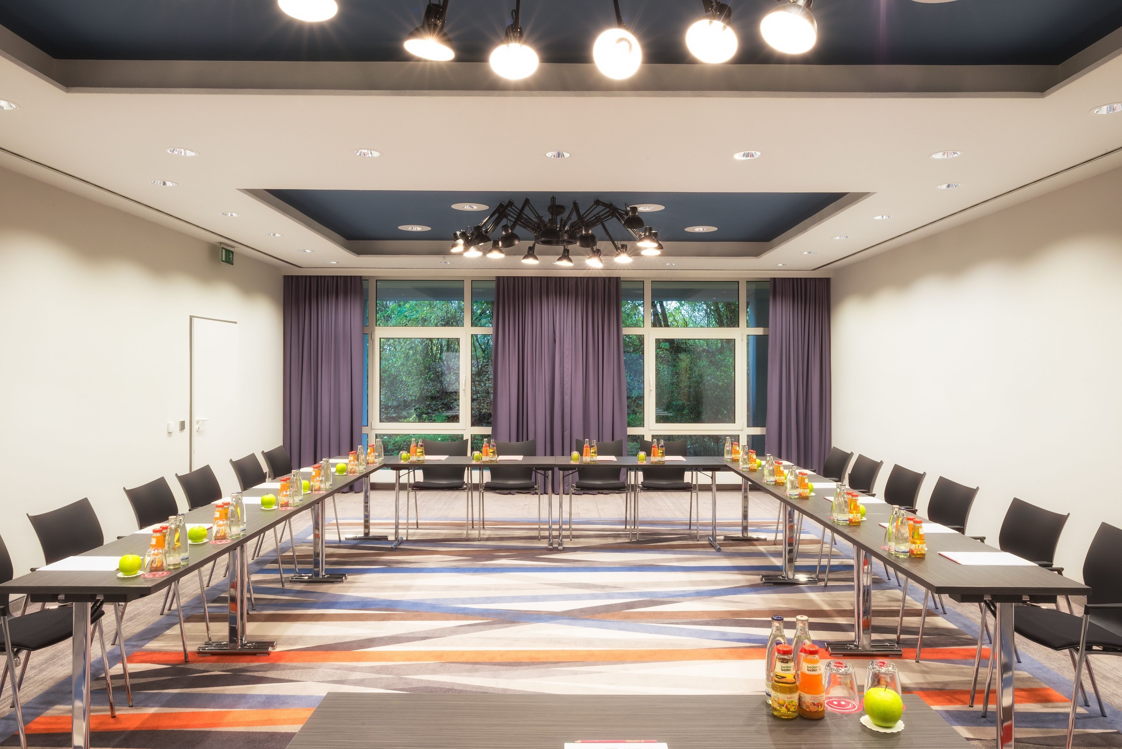 Una sala conferenze con un lungo tavolo, sedie e una tappezzeria a motivi.