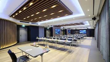 Une salle de conférence moderne, dotée de longues tables, de chaises et d’une scène avec des écrans.