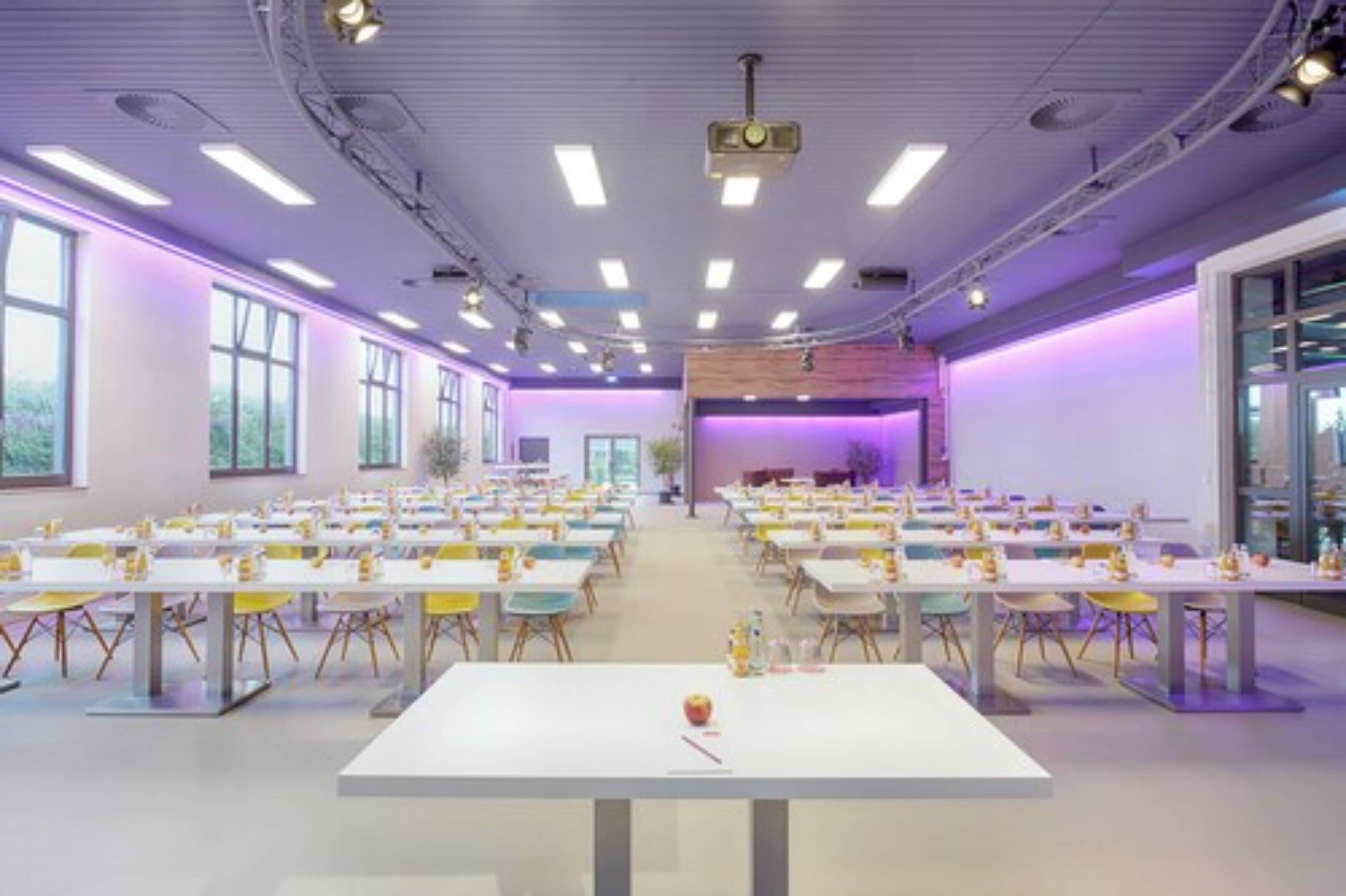 A conference room with multiple tables and chairs, large windows, and a stage area.