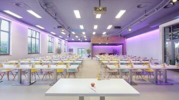 A conference room with multiple tables and chairs, large windows, and a stage area.