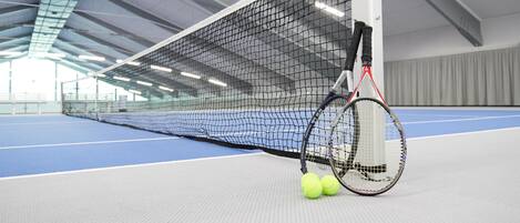 An indoor tennis court with a net, tennis rackets, and balls.