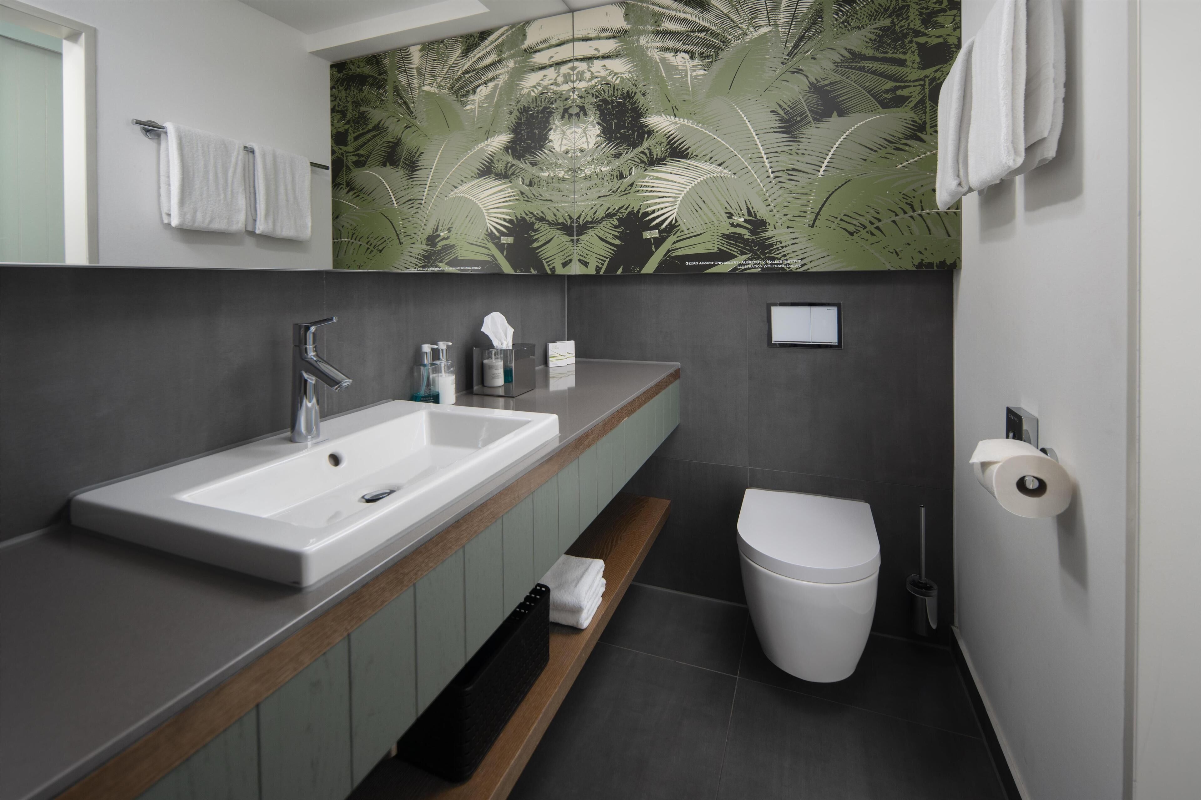 A modern bathroom with a large sink, toilet, and a decorative wall mural.