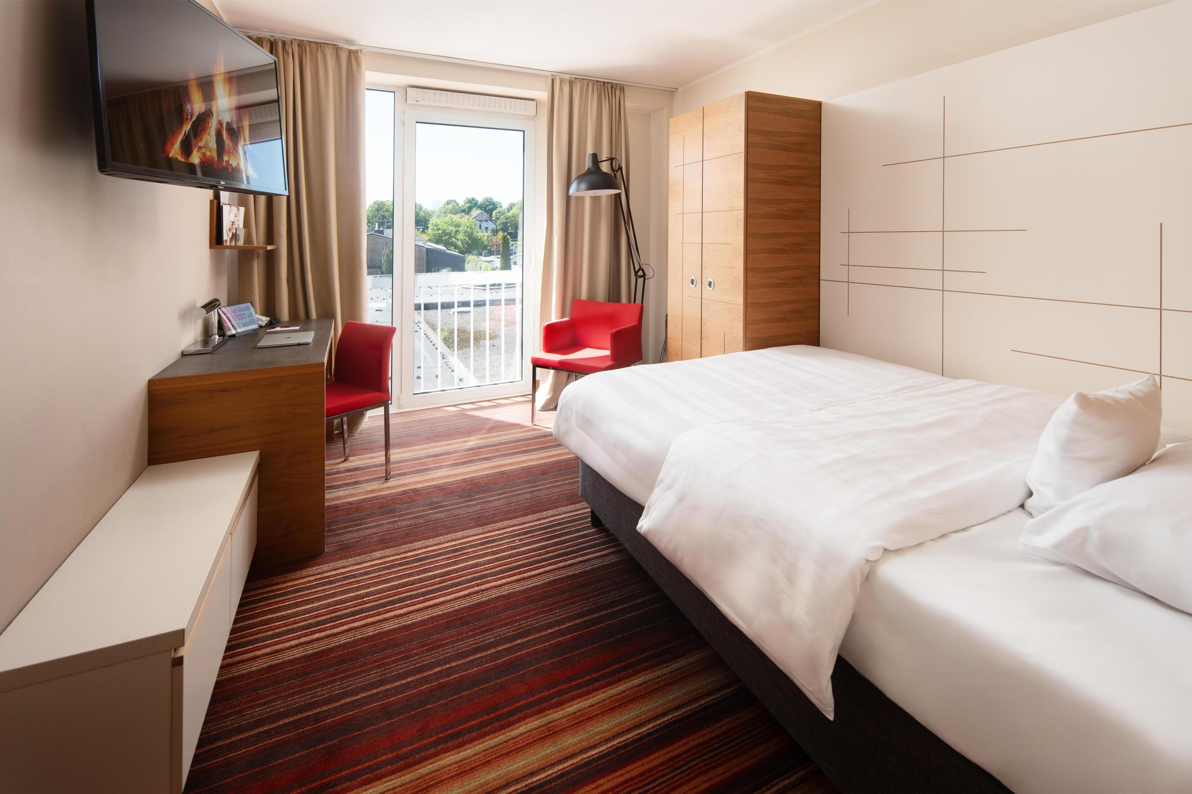 Habitación de hotel con cama, escritorio, silla, televisión y vista al exterior.