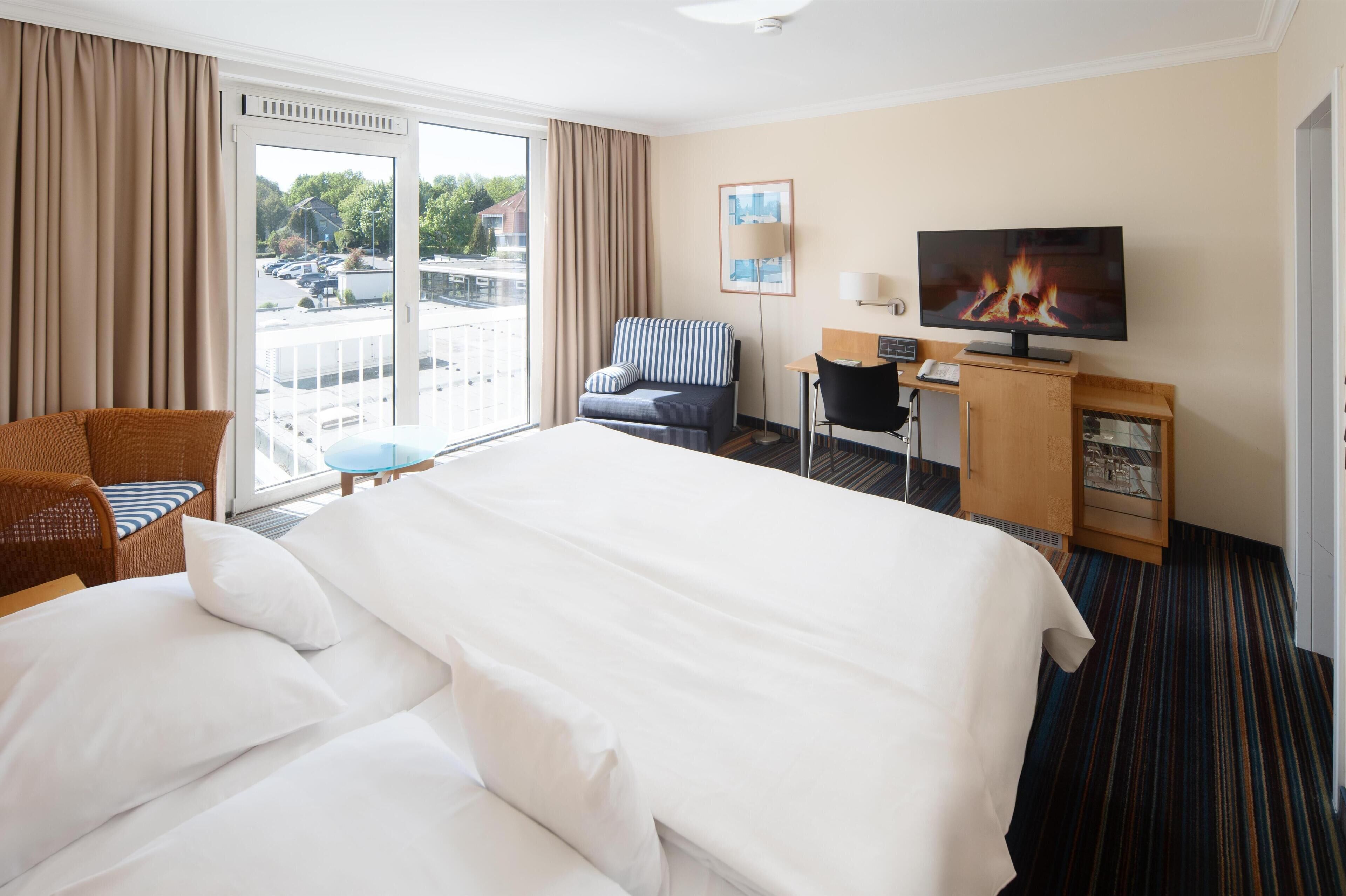 Habitación de hotel con una cama grande, un escritorio, una silla, un televisor y vistas al exterior.