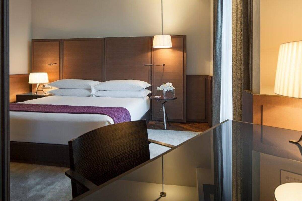Quarto de hotel com cama, mesas de cabeceira, uma cadeira e um espelho.