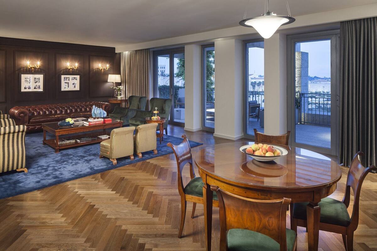 Uma sala de estar espaçosa com um sofá de couro, uma mesa de jantar com cadeiras e vista para a cidade através de amplas janelas.