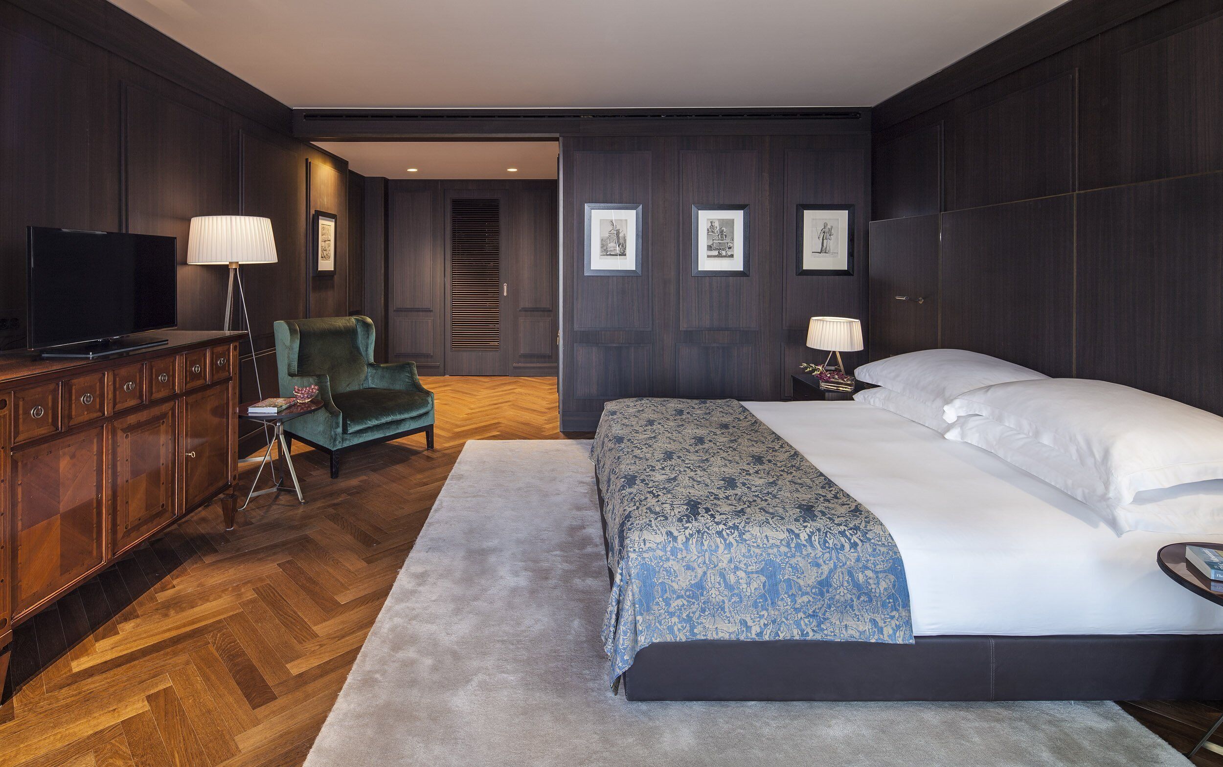 Una habitación de hotel moderna con una cama grande, un televisor, un sillón verde y un aparador de madera.