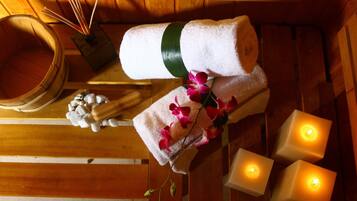 A wooden room with a wooden tub, a white towel, pink flowers, and three lit candles.