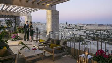 A terrace with outdoor seating, a view of the city, and a stone pillar.