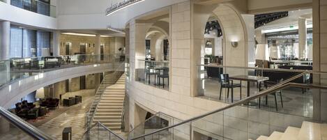 A multi-level hotel lobby with a central staircase, glass railings, and modern furnishings.