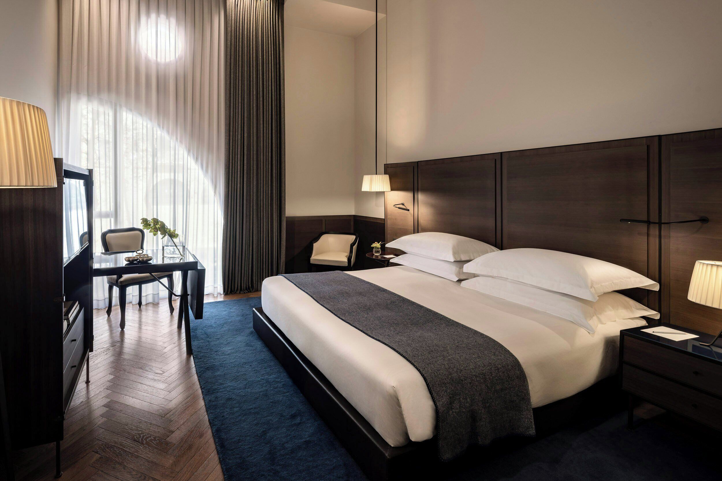 A hotel room with a large bed, a desk with a chair, a nightstand, and a lamp.