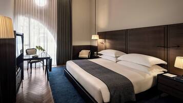 A hotel room with a large bed, a desk with a chair, a nightstand, and a lamp.