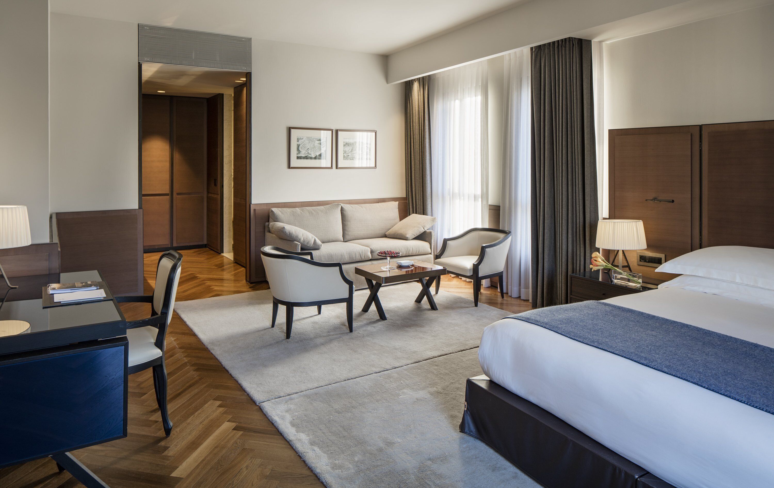 A hotel room with a bed, a desk, a sofa, two armchairs, a coffee table, and a nightstand.