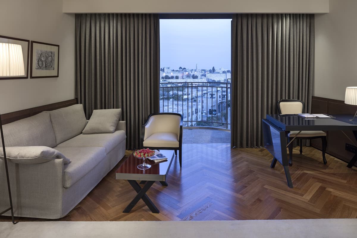 Quarto de hotel com varanda, um sofá, uma cadeira, uma mesa de escritório e uma mesa de centro.