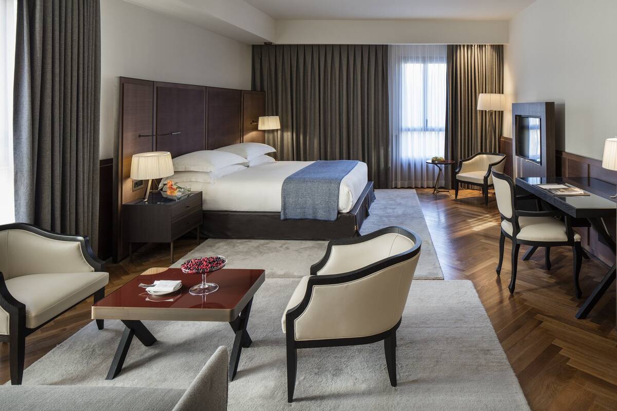 Quarto de hotel com cama, mesas de cabeceira, escrivaninha, cadeira e televisão.