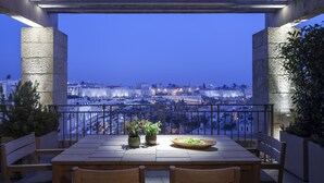 A terrace with a table and chairs, potted plants, and a view of a cityscape at dusk. - The David Citadel Jerusalem (Jerusalem)