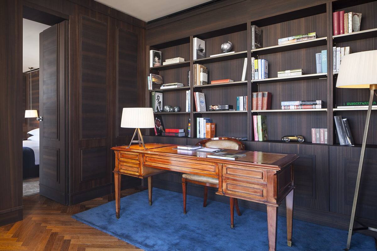 Sala de estudos com uma mesa de madeira, estantes e um tapete azul.