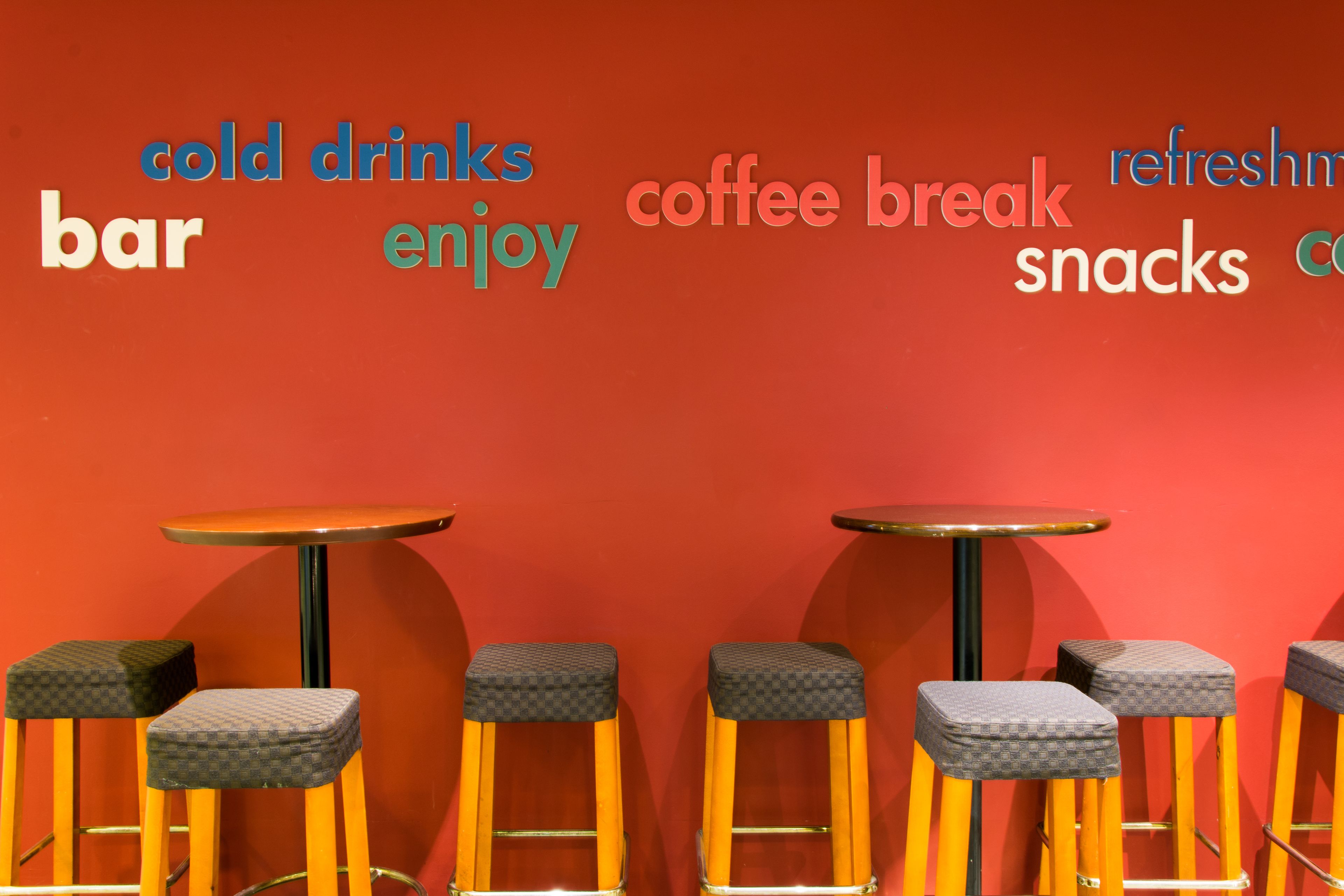 A bar area with stools and tables, and words like "cold drinks," "coffee break," and "snacks" on the wall.