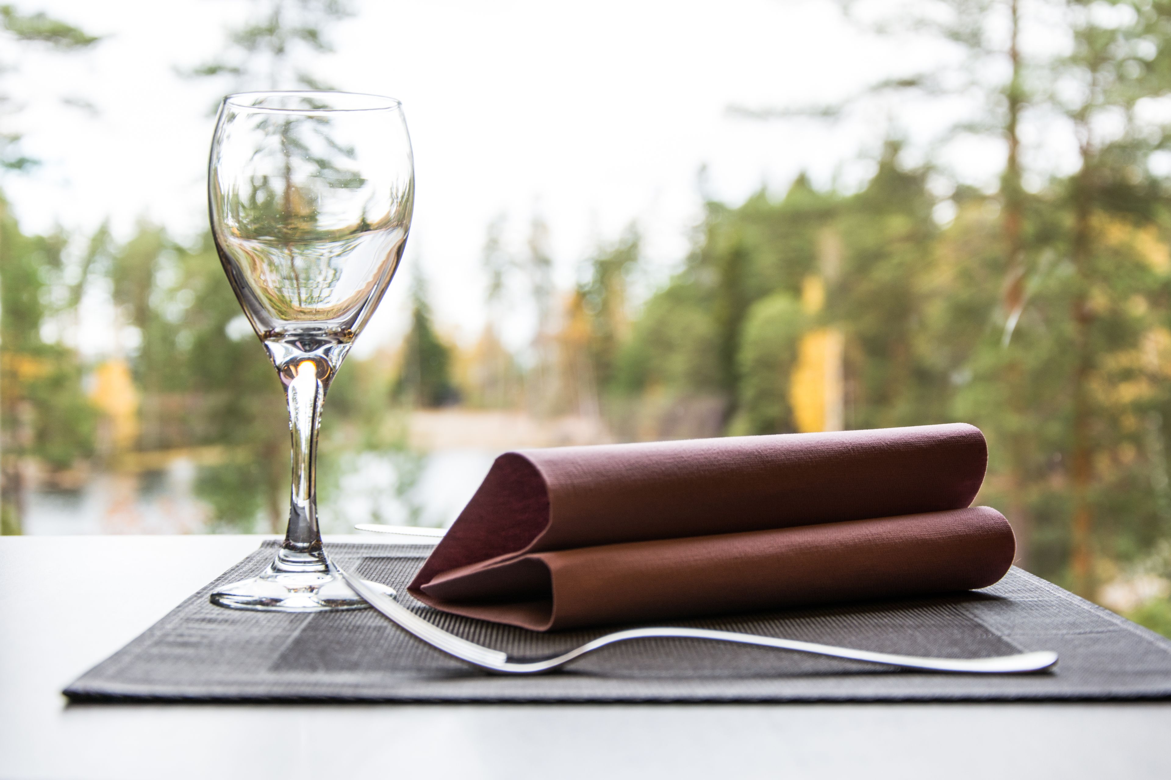 Une table avec un verre de vin blanc, une serviette pliée et une cuillère posée sur un set de table.