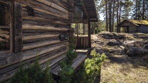 Una cabaña rústica de troncos con un porche, rodeada por un bosque.