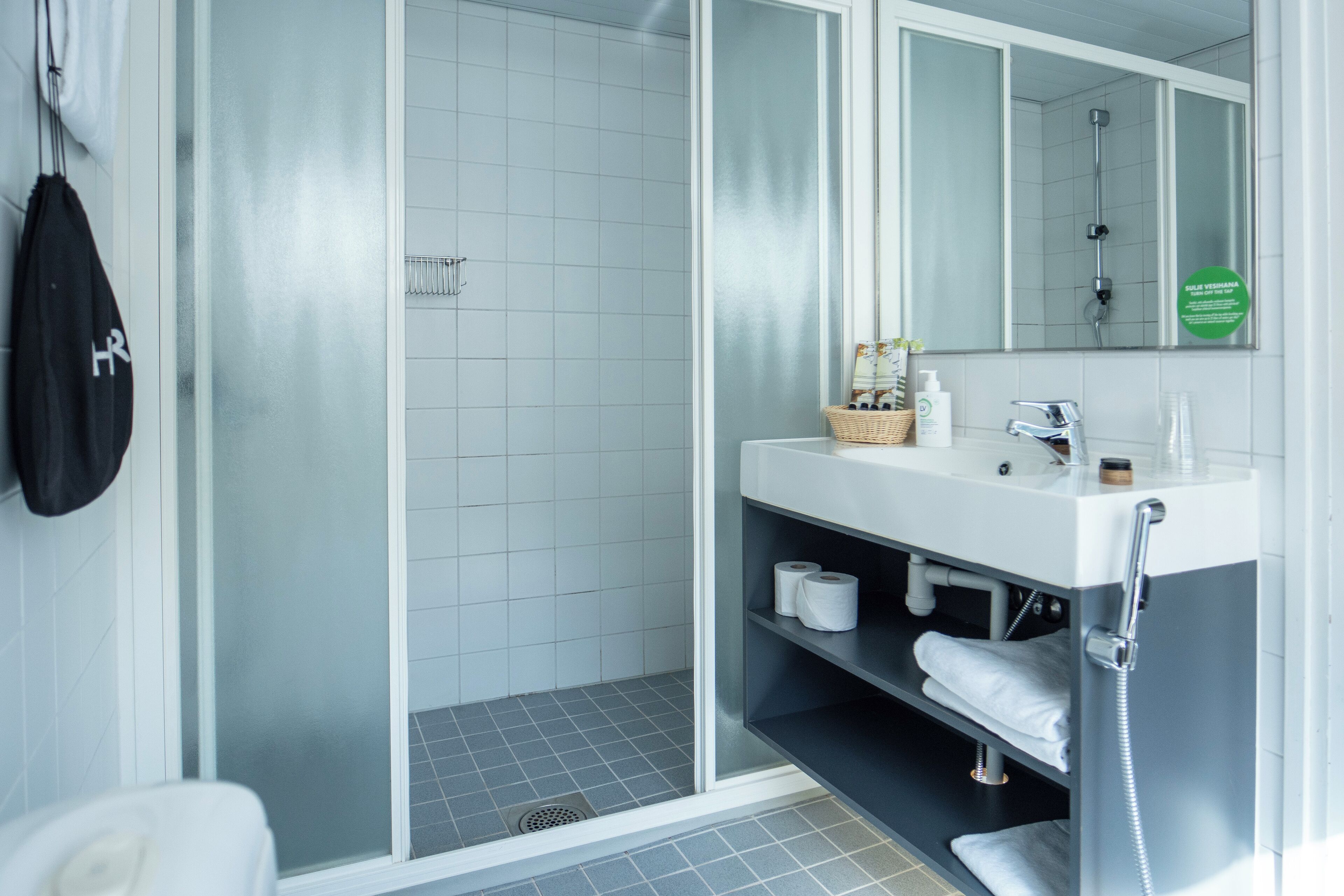Ein modernes Badezimmer mit einer Duschkabine aus Glas, einem weißen Waschbecken mit Spiegel und einer Ablage mit Handtüchern und Pflegeprodukten.