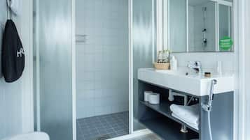 Ein modernes Badezimmer mit einer Duschkabine aus Glas, einem weißen Waschbecken mit Spiegel und einer Ablage mit Handtüchern und Pflegeprodukten.