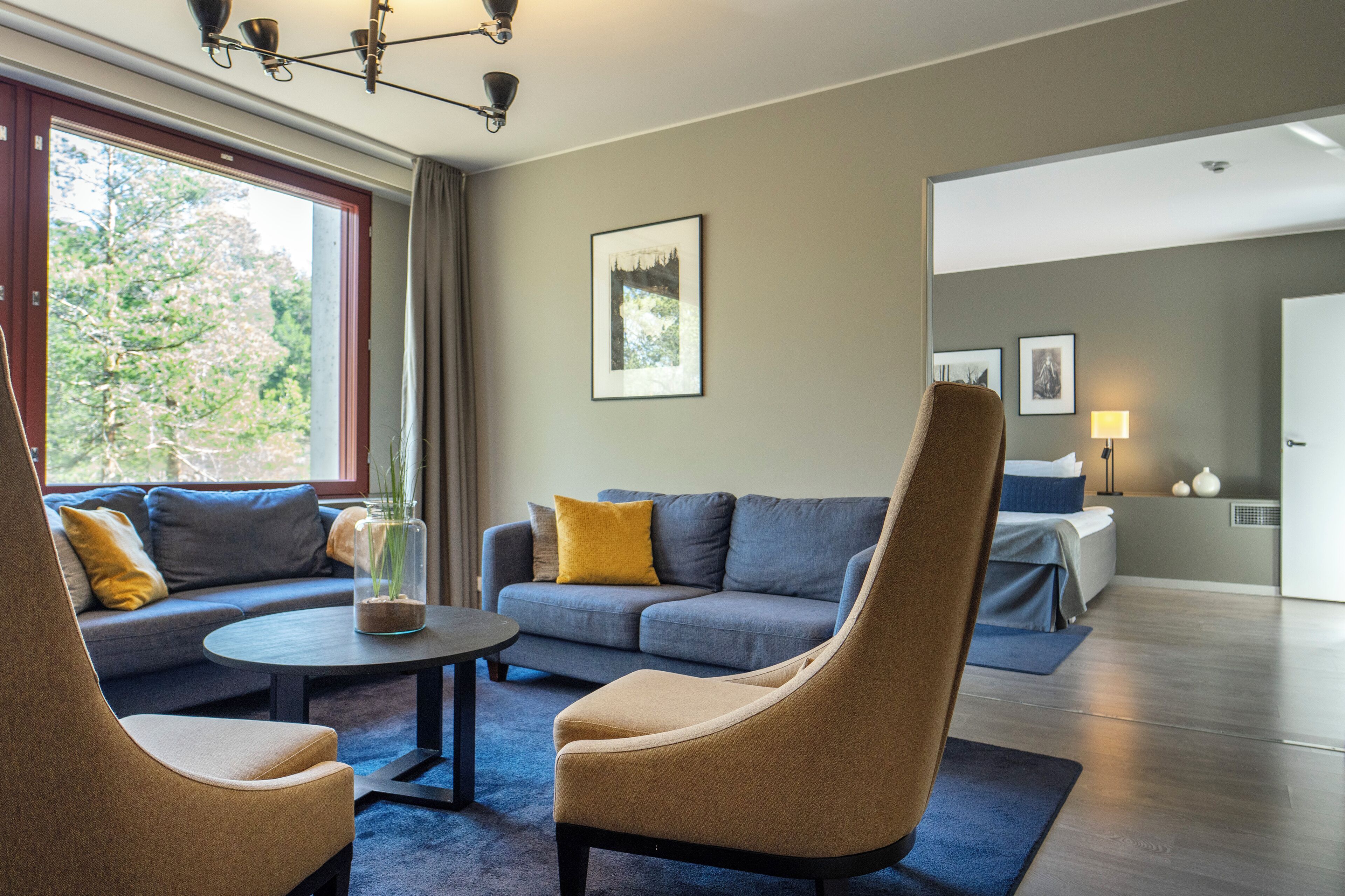 A modern hotel room with a sofa, armchairs, a coffee table, and a bed.