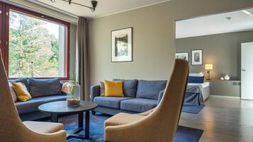 A modern hotel room with a sofa, armchairs, a coffee table, and a bed.