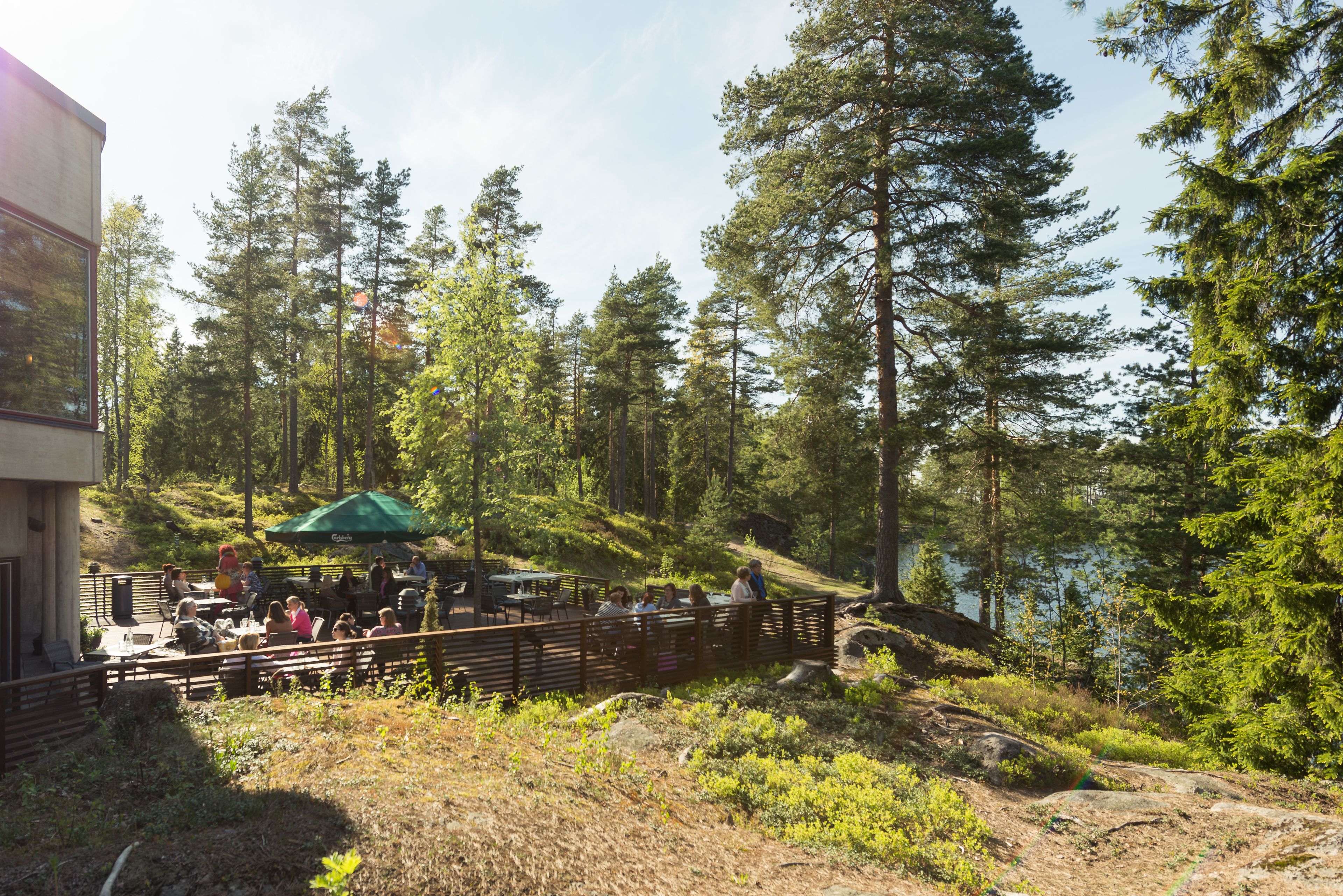 Een buitenterras met tafels en stoelen, omgeven door bomen en uitzicht op een meer.