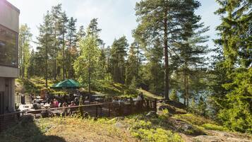 Een buitenterras met tafels en stoelen, omgeven door bomen en uitzicht op een meer.