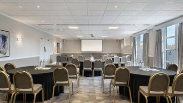 Una sala conferenze con un grande tavolo ovale, diverse sedie, uno schermo per proiettore e un pavimento rivestito di moquette.