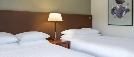 Habitación de hotel con dos camas, una mesita de noche con lámpara y una obra de arte enmarcada en la pared.