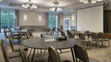 Un salón de conferencias con mesas redondas, sillas y una pantalla para proyector.