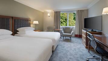 A hotel room with two beds, a desk with a television, a chair, and a window with curtains.