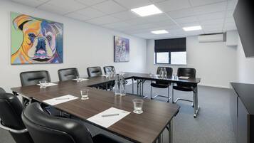 A conference room with a long table, black chairs, and two paintings on the walls.