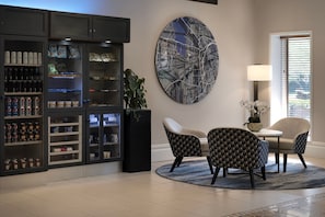 A modern living room with a round coffee table, two patterned armchairs, a large abstract wall art, a built-in entertainment unit with snacks, and a potted plant.