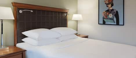 Een net opgemaakt bed met witte lakens, een houten hoofdbord en twee bedlampjes.