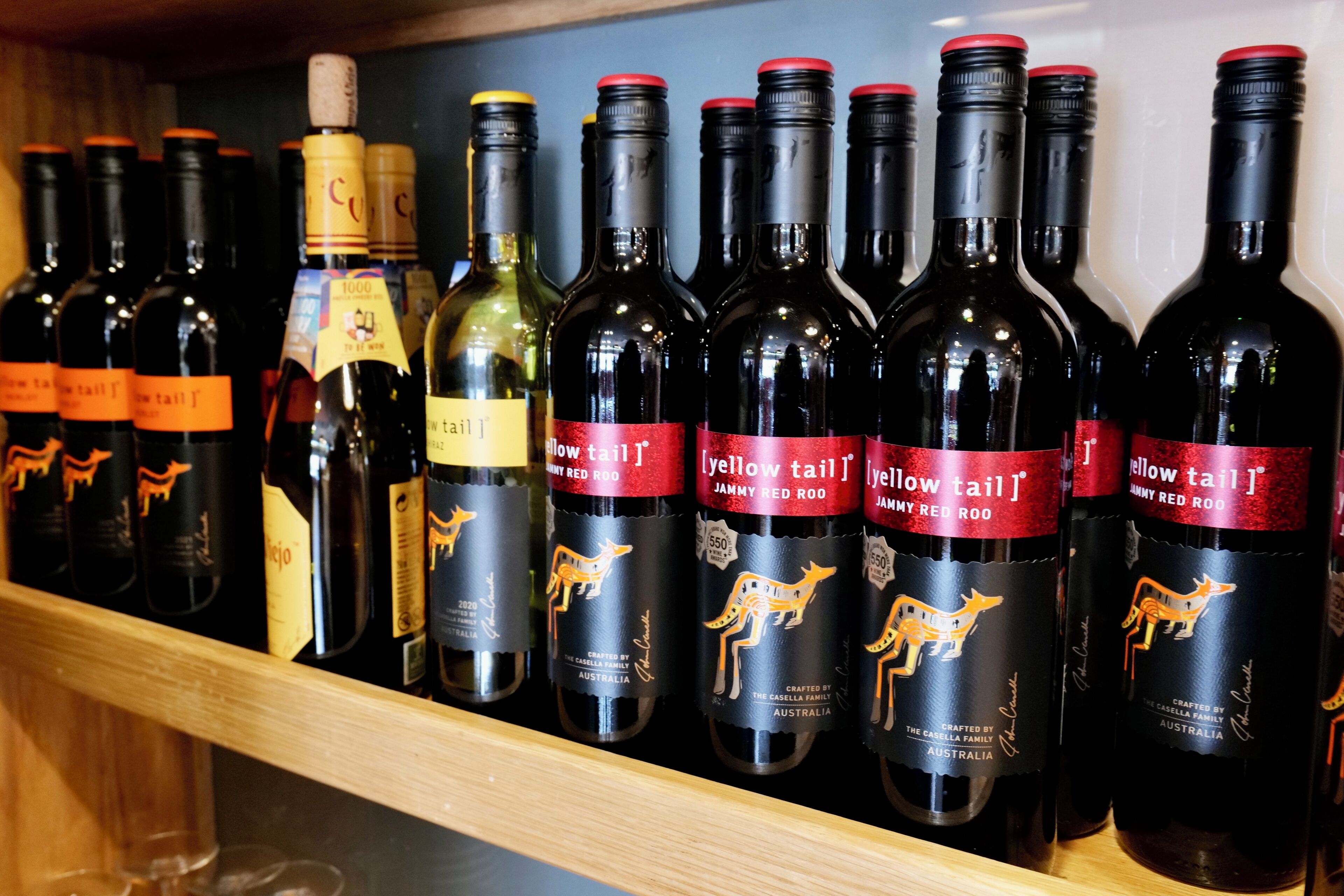 Ein Regal mit verschiedenen Weinflaschen, einige beschriftet mit 'Yellow Tail' und andere mit 'Jammy Red Roo'.