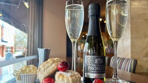 Una mesa servida con una botella de Prosecco, dos copas de champán y un plato de scones con cerezas.