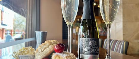 A table setting with a bottle of Prosecco, two glasses of champagne, and a plate of scones with cherries.