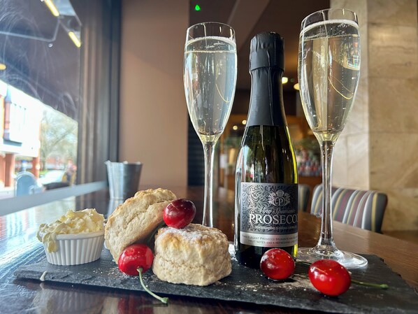 A table setting with a bottle of Prosecco, two glasses of champagne, and a plate of scones with cherries.