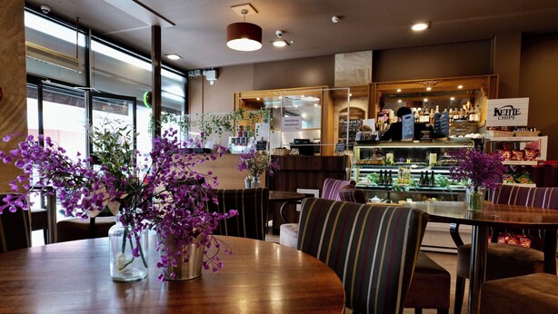 Un restaurante con mesas y sillas de madera, una zona de bar con un letrero que dice 'Kettle Chips' y una vitrina con productos alimenticios.