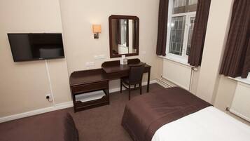 A hotel room with a bed, a desk, a chair, a TV, and a window with curtains.