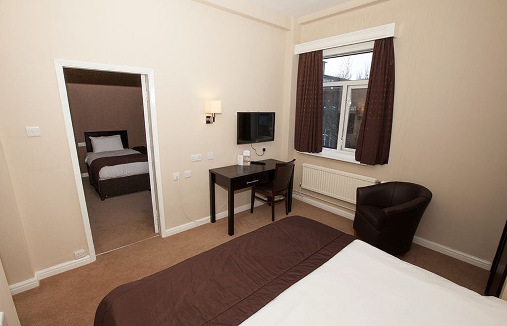 A hotel room with a bed, a desk, a chair, a TV, and a window with curtains.