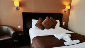 Habitación de hotel con una cama grande, dos lámparas fijadas a la pared, un cabecero oscuro y un sillón de cuero marrón.